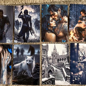 May include: A collection of fantasy art prints featuring various scenes. The images depict figures in armor, romantic couples, a white fox, a castle, and a sword with a butterfly. The color palette includes blues, grays, and whites.