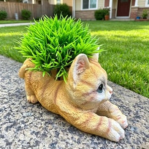 Könnte beinhalten: Ein orangefarbener Tabby-Katzen-Pflanztopf mit grünem Kunstgras. Die Katze liegt ausgestreckt. Der Pflanztopf besteht aus einem haltbaren Material. Geeignet für den Innen- und Außenbereich. Ca. 25 cm lang.