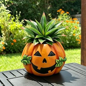 May include: A bright orange ceramic jack-o'-lantern planter featuring a carved face with black triangular eyes and a wide, toothy grin. Two sculpted green leaves are attached to the sides. A spiky green agave plant sits inside the pumpkin.