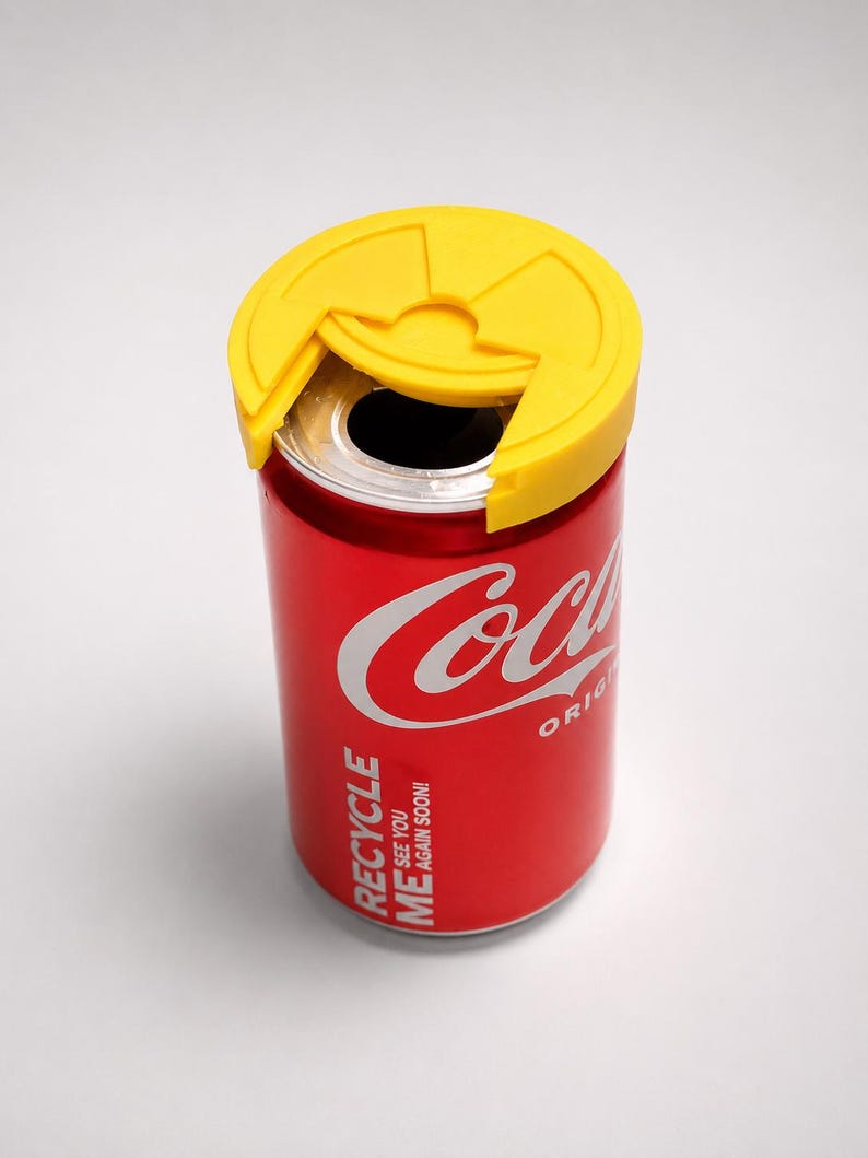 Puede incluir: Una lata roja de Coca-Cola con una tapa amarilla. La lata tiene el logotipo de Coca-Cola en blanco y las palabras "RECYCLE ME SEE YOU AGAIN SOON!" impresas en el lateral. La tapa amarilla est&aacute; dise&ntilde;ada para cubrir la abertura de la lata.