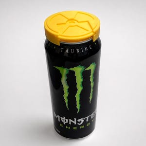 Puede incluir: Una lata negra de bebida energ&eacute;tica Monster con tapa amarilla. La lata presenta el logotipo de Monster en verde y la palabra "TAURINE" en blanco. La lata es cil&iacute;ndrica y se alza sobre un fondo blanco.