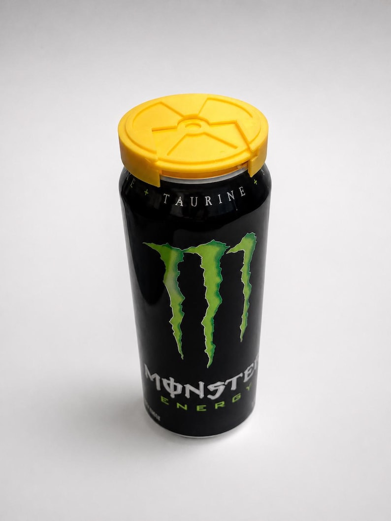 Puede incluir: Una lata negra de bebida energ&eacute;tica Monster con tapa amarilla. La lata presenta el logotipo de Monster en verde y la palabra "TAURINE" en blanco. La lata es cil&iacute;ndrica y se alza sobre un fondo blanco.