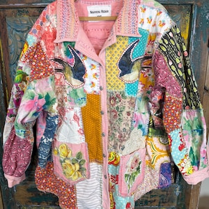 Könnte beinhalten: Eine langärmelige Knopfjacke aus einem Patchwork verschiedener floraler, geometrischer und einfarbiger Stoffe. Das Kleidungsstück verfügt über zwei Vordertaschen, einen Kragen mit sichtbaren Nähten und Schwalbenmotive. Ein Etikett trägt die Aufschrift Nouveau Redux.
