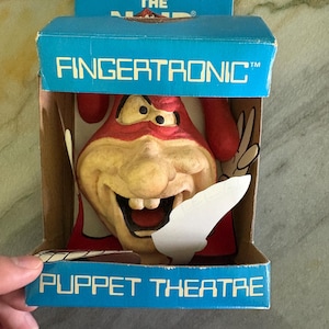 Peut inclure: Un jouet FingerTronic Puppet Theatre vintage dans sa boîte d'origine. La boîte bleue avec du texte blanc présente une marionnette rouge et beige avec un grand sourire édenté. La boîte indique "FingerTronic" et "Puppet Theatre".