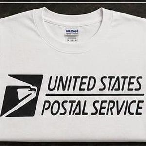 Könnte beinhalten: Ein weißes kurzärmeliges T-Shirt mit dem schwarzen United States Postal Service Logo und Schriftzug auf der Vorderseite. Die Grafik zeigt ein stilisiertes Adlerkopf-Symbol in einem schwarzen Quadrat sowie den Text United States Postal Service.