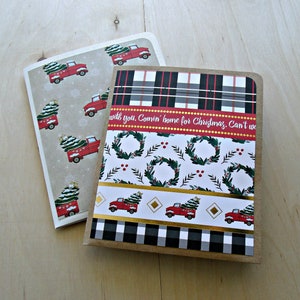 Puede incluir: Dos cuadernos con temática navideña. Uno presenta un patrón de camiones rojos que transportan árboles de Navidad sobre un fondo beige. El otro tiene un diseño a cuadros, un patrón de coronas y el texto "Comin' home for Christmas".