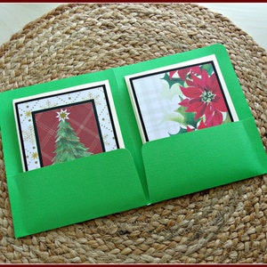 Peut inclure: Un porte-cartes de Noël vert avec deux poches, chacune contenant une carte décorative. Une carte présente un motif de sapin de Noël, l'autre une fleur de poinsettia. Les cartes sont encadrées de bordures noires et blanches.