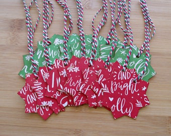May include: A collection of star-shaped gift tags in red and green, with white lettering and snowflake designs. The tags are strung with red, white, and green twine. The text on the tags reads "Merry and Bright" and "Jolly".