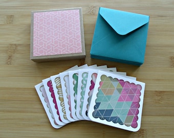Op de afbeelding: Een set van acht blanco wenskaarten met gegolfde randen en kleurrijke geometrische patronen. De kaarten zijn verpakt in een bruine doos met een roze geometrisch patroon en worden geleverd met turquoise enveloppen.