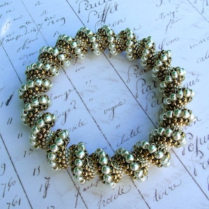 Puede incluir: Un brazalete de cuentas plateadas y doradas con un diseño en espiral. El brazalete está hecho de pequeñas cuentas redondas que están tejidas juntas en un patrón en espiral. Las cuentas son una mezcla de plata y oro, creando un hermoso contraste.