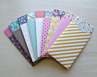 May include: A set of ten colorful paper envelopes with different patterns, including polka dots, stripes, and floral designs. The envelopes are arranged in a fan shape, with the yellow and white striped envelope in the front.