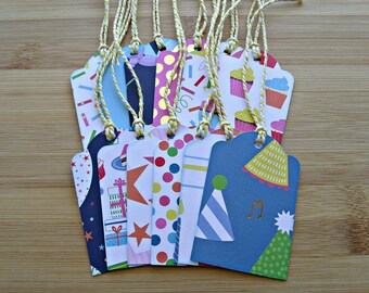 May include: A set of 12 colourful gift tags with various birthday themes, including cupcakes, confetti, party hats, and musical notes. Each tag has a gold string attached.