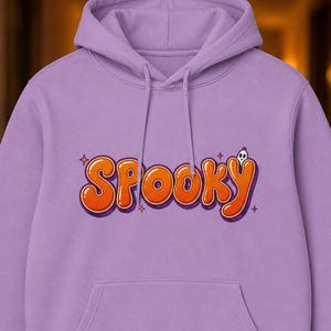 Peut inclure: Un sweat-shirt à capuche violet clair avec une poche kangourou sur le devant et des manches longues. Le centre de la poitrine affiche le mot SPOOKY dans une police orange audacieuse de style bulle avec un contour violet foncé et un petit fantôme.