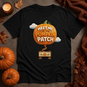 Peut inclure: Un t-shirt noir orné d'un grand graphique de citrouille orange avec le texte "MEET ME AT THE PUMPKIN PATCH" en lettres blanches. Sous la citrouille, un ruban relie un petit panneau en bois affichant une illustration de citrouille.