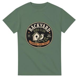 Puede incluir: Camiseta verde con un gráfico circular que presenta una casa para pájaros, un pájaro y el texto "Backyard Bird Club". El diseño incluye las palabras "Birdwatch, Listen, Repeat" y "Early Mornings".