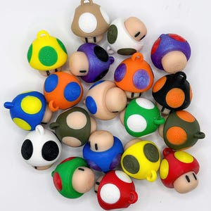 Può includere: Una collezione di figurine a forma di fungo con varie combinazioni di colori, tra cui giallo, blu, arancione, verde e rosso. Ogni fungo ha un motivo a pois unico e un piccolo anello sulla parte superiore.