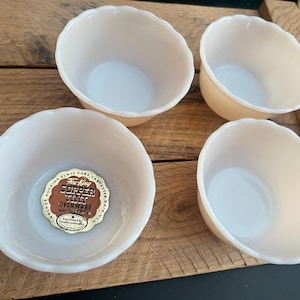 May include: Four vintage, off-white glass bowls with scalloped edges. One bowl has a gold and brown sticker that reads "Copper Tint Ovenware". The bowls are on a wooden tray.