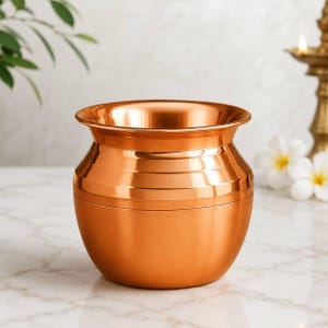 Op de afbeelding: Een gepolijste koperen pot met een brede, uitlopende rand en een afgerond lichaam. Het vat heeft een gladde, metalen afwerking met subtiele horizontale banden rond het bovenste gedeelte, wat zorgt voor een reflecterend oppervlak.