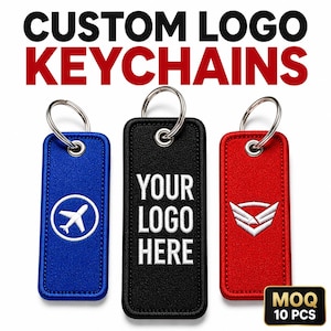 Könnte beinhalten: Drei rechteckige bestickte Schlüsselanhänger mit Metallringen. Der blaue zeigt ein weißes Flugzeugsymbol, der schwarze den weißen Text YOUR LOGO HERE und der rote ein weißes geflügeltes Emblem. Darüber steht der Text CUSTOM LOGO KEYCHAINS.