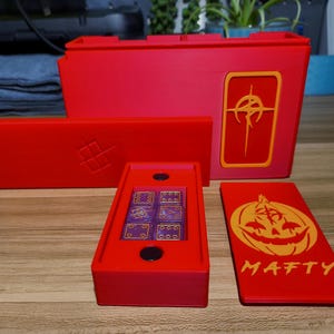 Puede incluir: Juego de accesorios de juego rojos, que incluye una caja de dados con dados morados, una tarjeta con un diseño de calabaza y el nombre "MAFTY", y cajas de almacenamiento. El juego está diseñado para juegos de mesa.