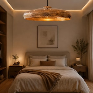 May include: A bedroom featuring a large, copper-colored pendant light fixture suspended above a bed. The bed is covered with neutral-toned bedding and a brown throw blanket. Two nightstands flank the bed, each with a lamp and decorative items.