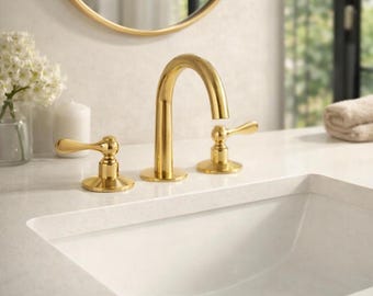 May include: A polished gold bathroom faucet set featuring a high-arc spout and two separate lever handles mounted on a white countertop with an integrated white sink basin and a matching gold drain stopper, reflecting a clean and bright aesthetic.