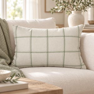 May include: A rectangular throw pillow featuring a light beige fabric base with a prominent sage green grid pattern. The pillow has a clean, structured design with thin, intersecting vertical and horizontal lines forming a classic plaid check motif.