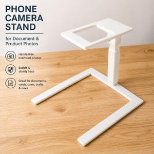 Puede incluir: Un soporte blanco para c&aacute;mara de tel&eacute;fono para documentos y fotos de productos. El soporte tiene una parte superior rectangular con un centro transparente, un soporte vertical ajustable y una base resistente. El texto en la imagen dice "PHONE CAMERA STAND".