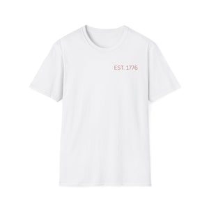 Op de afbeelding: Een wit T-shirt met ronde hals en korte mouwen. De tekst "EST. 1776" is in het rood gedrukt op de bovenborst. Het shirt is gemaakt van een zacht, lichtgewicht materiaal.