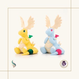 May include: Two handmade figurines of a dragon-like creature. One is yellow with green and cream accents, the other is light blue with red and cream accents. Both have large cream-colored antlers and are sitting down.