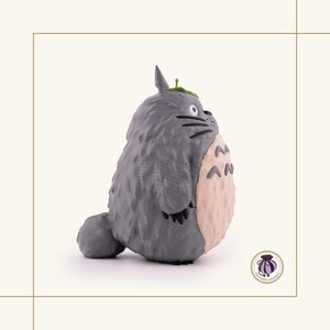 K&ouml;nnte beinhalten: Graue Totoro-Figur, eine Figur aus dem Zeichentrickfilm Mein Nachbar Totoro. Die Figur hat einen hellbeige Bauch, schwarze Schnurrhaare und ein kleines gr&uuml;nes Blatt auf dem Kopf. Die Figur steht vor wei&szlig;em Hintergrund.