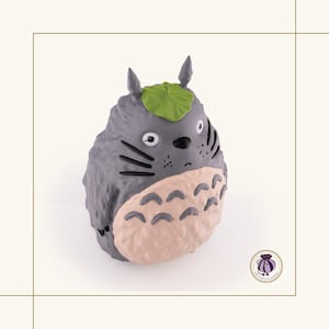 K&ouml;nnte beinhalten: Graue Totoro-Figur mit hellrosa Bauch und gr&uuml;nem Blatt auf dem Kopf. Die Figur hat schwarze Schnurrhaare und kleine, spitze Ohren. Ein Sammlerst&uuml;ck.