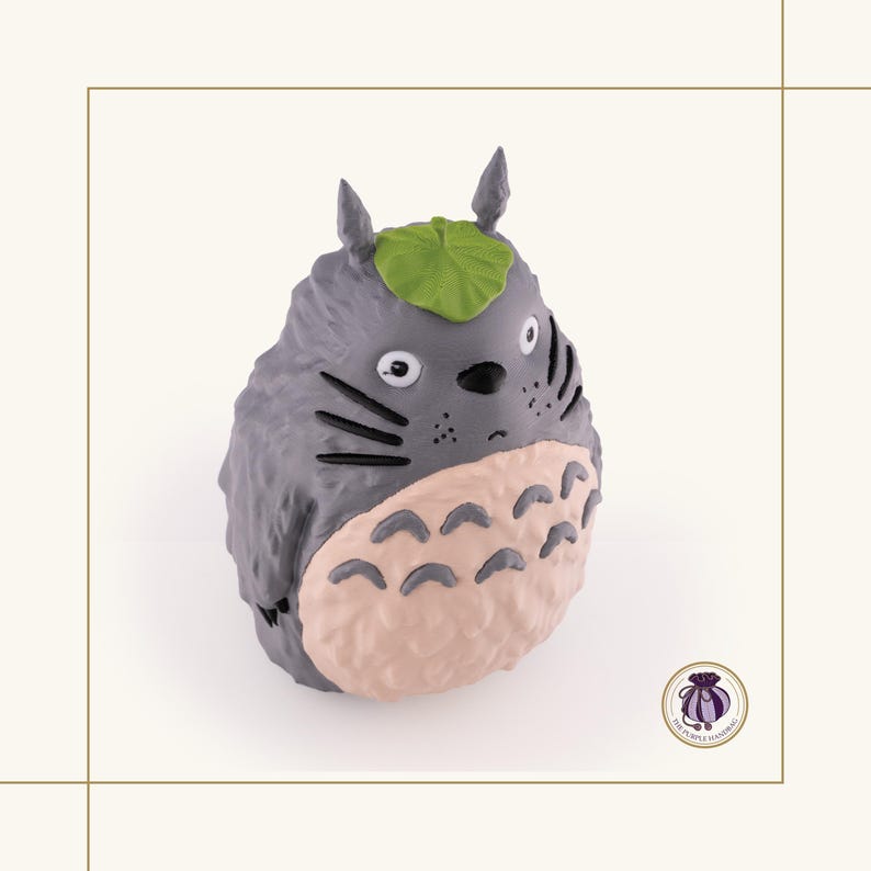 K&ouml;nnte beinhalten: Graue Totoro-Figur mit hellrosa Bauch und gr&uuml;nem Blatt auf dem Kopf. Die Figur hat schwarze Schnurrhaare und kleine, spitze Ohren. Ein Sammlerst&uuml;ck.