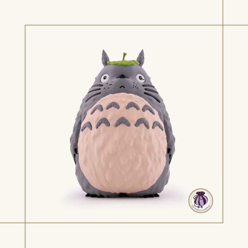 K&ouml;nnte beinhalten: Graue Figur von Totoro, einer Figur aus dem Zeichentrickfilm Mein Nachbar Totoro. Die Figur hat einen hellrosa Bauch, ein gr&uuml;nes Blatt auf dem Kopf und schwarze Schnurrhaare. Es ist ein Sammlerst&uuml;ck.