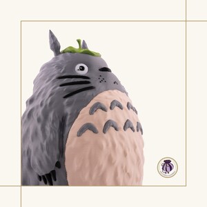 K&ouml;nnte beinhalten: Graue Figur von Totoro, einer Figur aus dem Zeichentrickfilm Mein Nachbar Totoro. Die Figur hat einen hellrosa Bauch, schwarze Schnurrhaare und ein gr&uuml;nes Blatt auf dem Kopf. Sammlerst&uuml;ck.