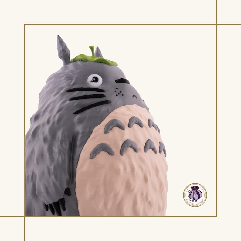 K&ouml;nnte beinhalten: Graue Figur von Totoro, einer Figur aus dem Zeichentrickfilm Mein Nachbar Totoro. Die Figur hat einen hellrosa Bauch, schwarze Schnurrhaare und ein gr&uuml;nes Blatt auf dem Kopf. Sammlerst&uuml;ck.