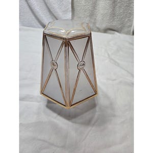 May include: A vintage, hexagonal-shaped lamp shade with a frosted glass design. The shade features gold-colored metal trim outlining the geometric panels and decorative circular accents. The top and bottom edges are also trimmed in gold.