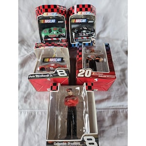 May include: A collection of NASCAR 2001 collectible ornaments and diecast cars. The items are in their original packaging, featuring race car models and figurines of drivers. The packaging is red and black with the NASCAR logo.