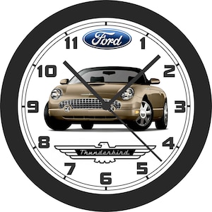 May include: Round wall clock with a black bezel, white face, and black numerals. The clock features a gold-colored Ford Thunderbird car in the center, with the Ford logo above and the Thunderbird logo below.