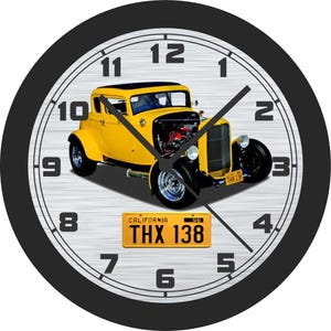 May include: Round wall clock with a black bezel and a silver-colored face. The clock face features a yellow classic car with the license plate "THX 138". Black clock hands point to the time.