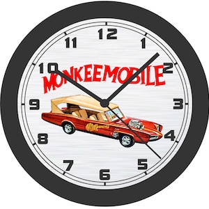 May include: Round wall clock with a black frame and a white face. The clock face features a red car with the text "MONKEEMOBILE" in red. The clock hands are black.