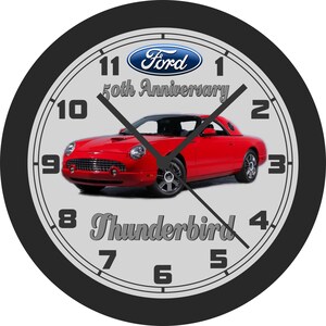 May include: Round wall clock with a black frame, featuring a red Ford Thunderbird car. The clock face has a light gray background with black numerals and hands. The Ford logo and "50th Anniversary" are displayed above the car, and "Thunderbird" is below.