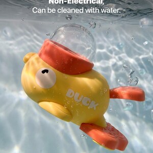 May include: A yellow toy duck with orange accents floats in water. The duck has a clear bubble on top and the word "DUCK" printed on its side. The text "Non-Electrical, Can be cleaned with water" is visible in the background.