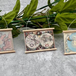 May include: Three rectangular wall hangings featuring vintage-style maps. Each piece is framed with light-colored wooden dowels at the top and bottom and includes a thin white string for hanging. The maps display different cartographic designs.