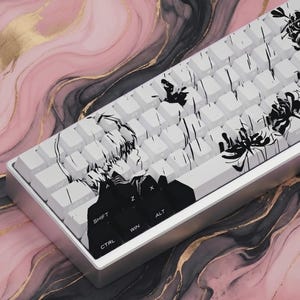 May include: A white mechanical keyboard with black and white artwork on the keycaps. The design includes a profile of a person and floral elements. The keyboard sits on a pink, black, and gold marble-patterned surface.
