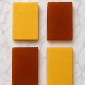 May include: Four rectangular blocks arranged in a two-by-two grid. Two blocks are a solid mustard yellow color with a smooth finish, and two blocks are a solid deep reddish-brown color with a smooth, glossy finish. Each block has rounded corners.