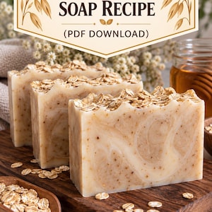 Può includere: Tre saponette rettangolari color beige con una consistenza marmorizzata e una copertura di avena intera. Il testo in alto recita Silk & Oat Soap Recipe (PDF Download). Un cucchiaio di legno pieno di avena poggia su un tagliere di legno.
