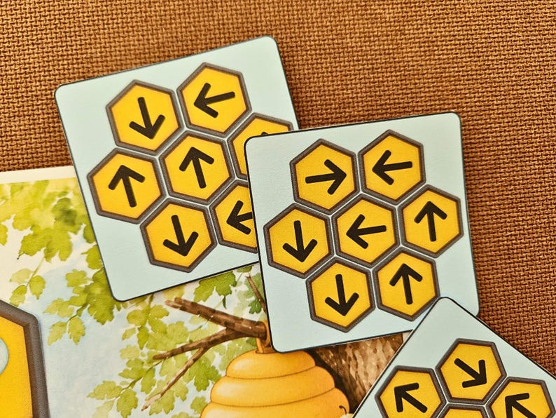 May include: Three square game tiles featuring a light blue background and a cluster of yellow hexagonal cells. Each hexagon contains a black arrow pointing in various directions, including up, down, left, and right, arranged in a honeycomb pattern.