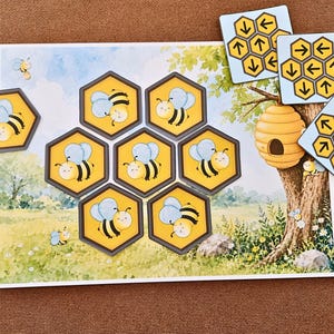 May include: A rectangular game board featuring a meadow scene with a tree and beehive, accompanied by seven hexagonal tiles depicting cartoon bees and three square tiles displaying yellow honeycomb patterns with black directional arrows.