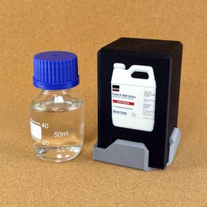 May include: A clear glass bottle with a blue screw cap and 50ml volume markings, positioned next to a black rectangular container featuring a white label that reads NATRON M03 PRIMER UV ADHESION PROMOTER BOSTON INDUSTRIAL SOLUTIONS 1L.